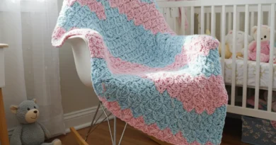 Soft pastel-colored crochet baby blanket made with shell stitch, folded neatly on a white nursery chair.